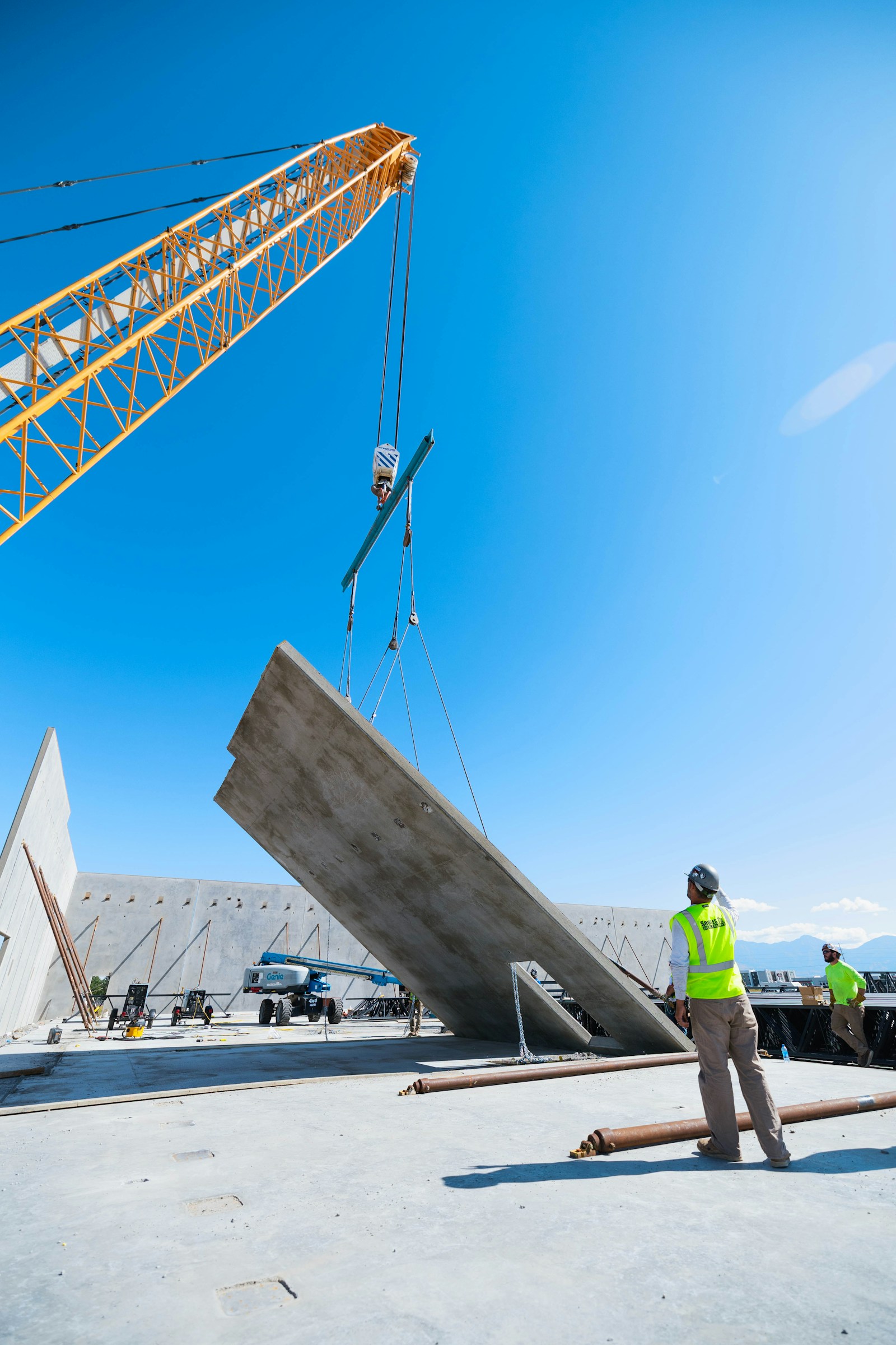 Construction workers overseeing a crane lifting a concrete wall panel into place